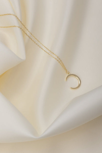 new crescent moon shaped pendant necklace on a gold chain. resting on a silk material